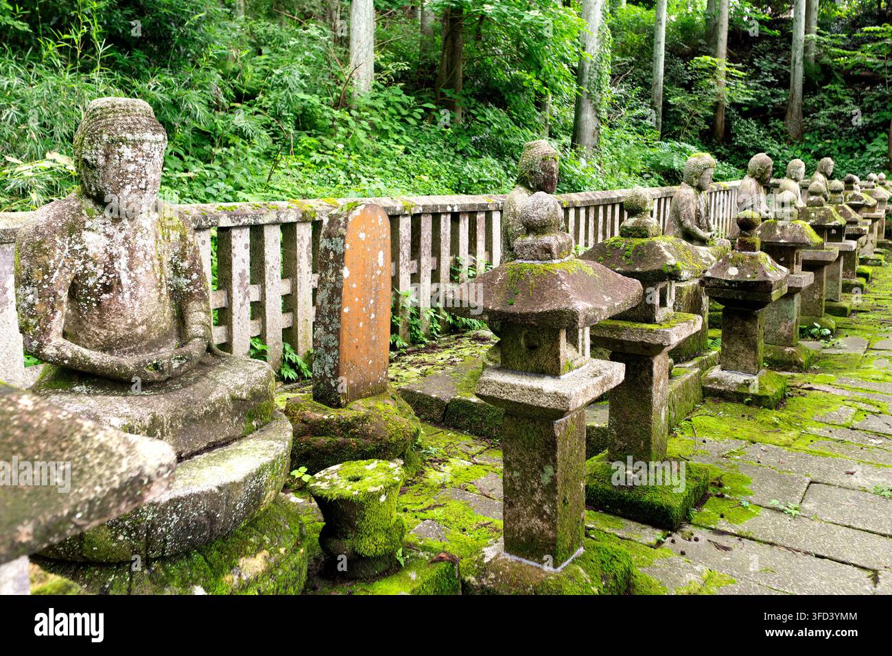 7. August 2022, Shiroishi, Miyagi, Japan: Steinstatuen und Steinlaternen, die mit üppigem grünem Moos bedeckt sind und das historische Mausoleum der Familie Katakura säumen Stockfoto
