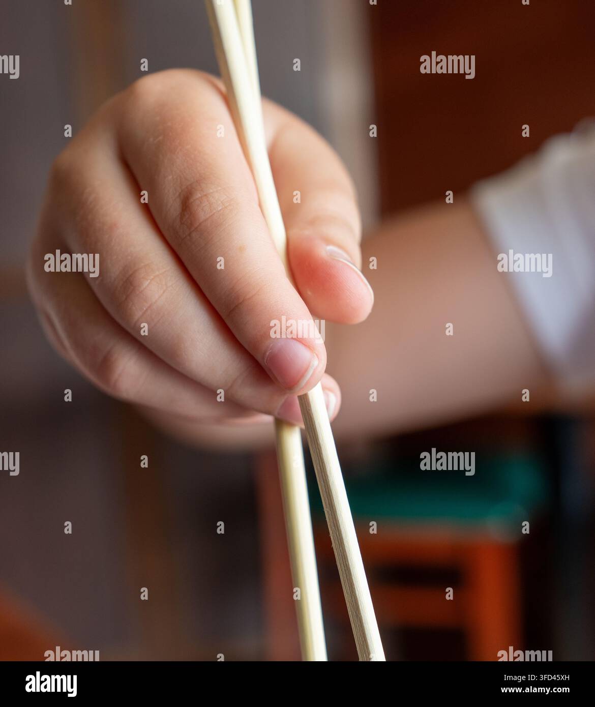 Vertikale Nahaufnahme einer Hand, die hölzerne Essstäbchen hält, während sie in einem Sushi-Restaurant isst. Schwache Tiefenschärfe hebt die Finger und Essstäbchen hervor Stockfoto