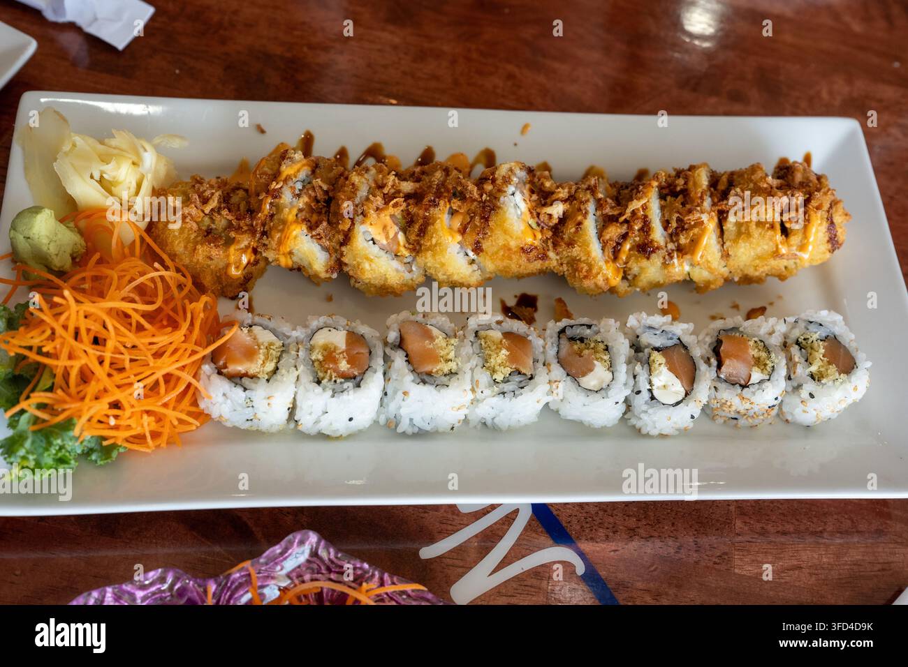 Nahaufnahme von verschiedenen Sushi-Rollen, die auf einem weißen rechteckigen Teller in einem japanischen Restaurant serviert werden. Das Tablett enthält Lachsrollen, knusprig gebratenes Sushi w Stockfoto