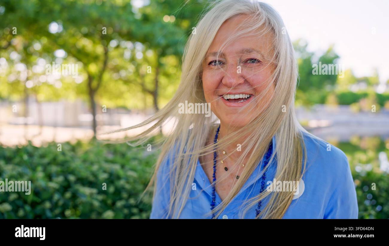 Seniorin lächelt mit im Wind wehenden Haaren im Freien im Park Stockfoto