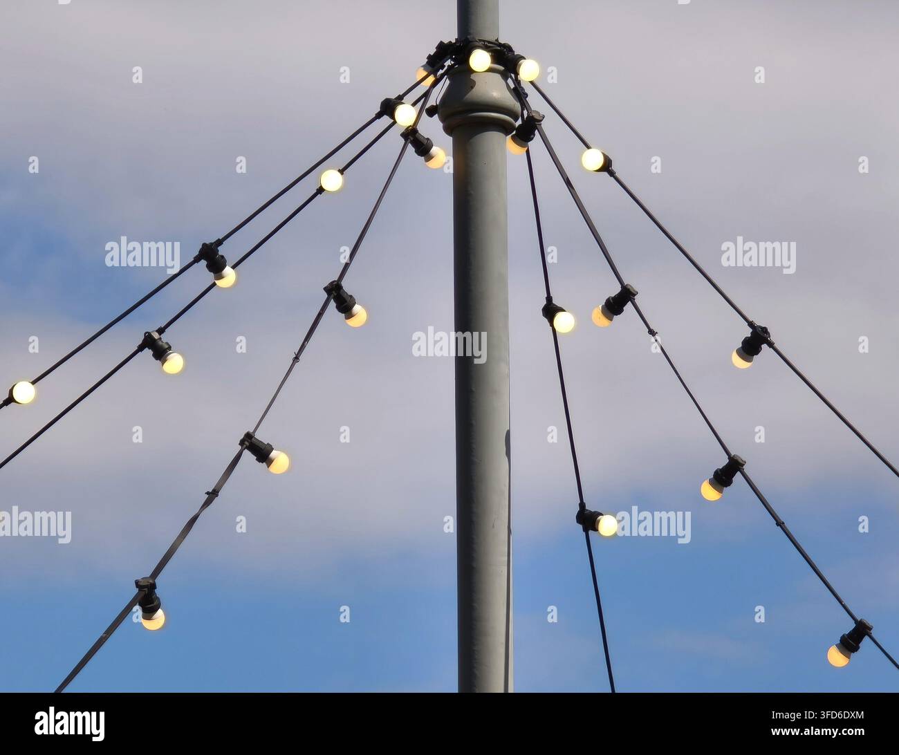 Lichterkette, die an einem Metallmast gegen einen blauen Himmel hängt. - Smartphone-aufgenommenes Stockfoto