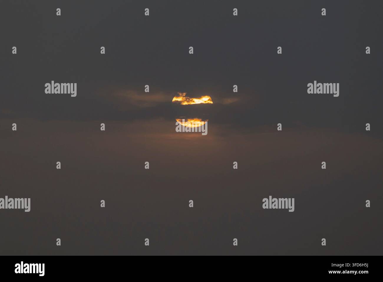 Die Sonne steht tief am Horizont während des Sonnenaufgangs und ist teilweise von einigen Wolkenschichten bedeckt Stockfoto