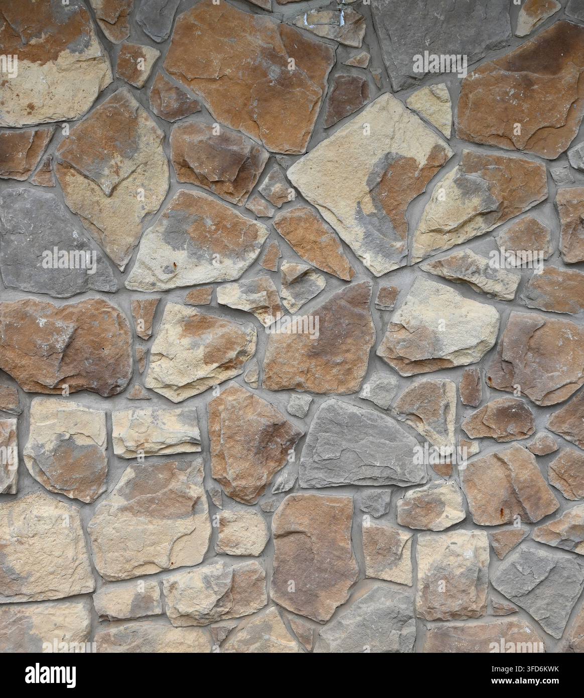 Nahaufnahme einer mehrfarbigen ebenen Mauerfläche aus Naturstein und Mörtel, die unterschiedliche Steingrößen und -formen in breitem, porösem, rissigem Mörtel zeigt Stockfoto