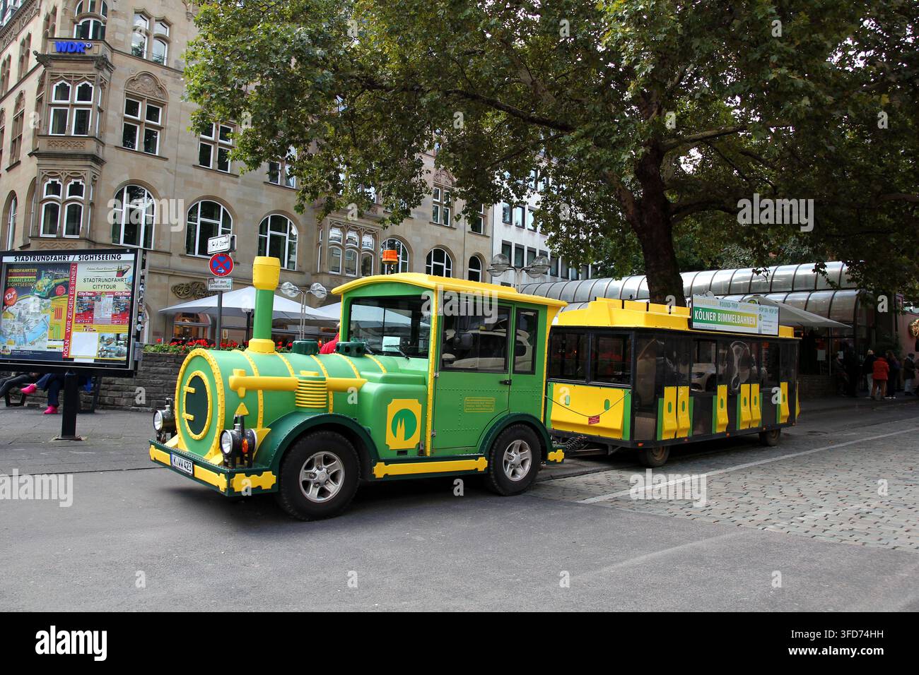 Grüne und gelbe Sightseeing-Touristenbahn auf einer Straße nahe dem Kölner Dom in Köln, Deutschland, die Stadtrundfahrten für Besucher und Touristen anbietet. Stockfoto