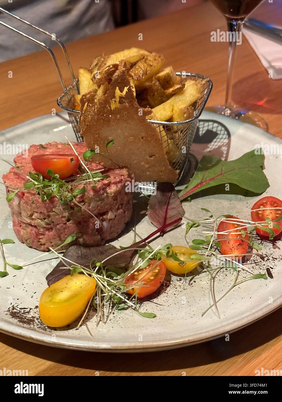 Gourmet-Rindfleisch-Tartare serviert mit knusprigen Pommes frites und frischen Kirschtomaten. Gourmet-Rindfleisch-Tartare schön angerichtet auf einer Keramikschale mit halbierten roten a - Smartphone-aufgenommenes Stockfoto