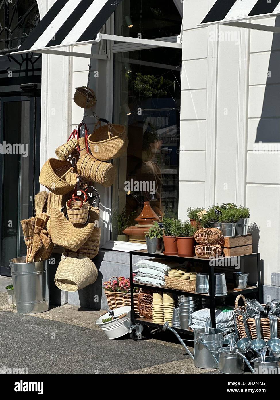 Ladengeschäft mit Weidenkörben, Topfpflanzen und Gartenbedarf. Charmante Schaufensterauslage mit handgefertigten Weidenkörben, die hängen - Smartphone-aufgenommenes Stockfoto