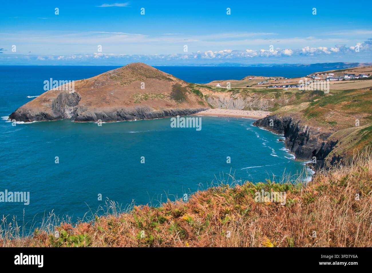 Weite Sommeraussicht auf den belebten Mwnt-Strand und dramatische Klippen in Ceredigion Wales unter einem lebendigen blauen Himmel Stockfoto