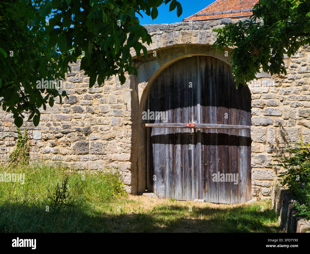 Rothenburg, Deutschland – 03.07.2026: Verwittertes Holztor in einem Steinbogen in Rothenburg, Deutschland, eingerahmt von Laubbäumen und Sommer sonnenschein Stockfoto