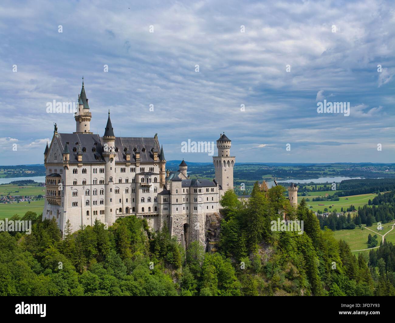 Neuschwanstein, Deutschland – 06. Jul 2026: Das Schloss Neuschwanstein erhebt sich über bewaldeten Hügeln und grünen Feldern in Neuschwanstein, Deutschland, unter einem dramatischen, wolkenverhangenen Himmel Stockfoto