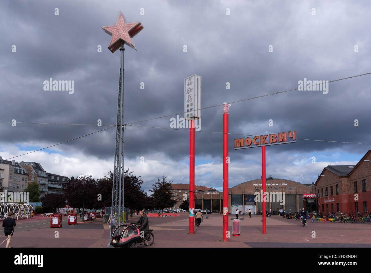 Besucher genießen den Roten Platz im Superkilen-Park von Kopenhagen, einem Zuhause internationaler Wahrzeichen wie des sowjetisch inspirierten Moskvich-Schildes. Stockfoto