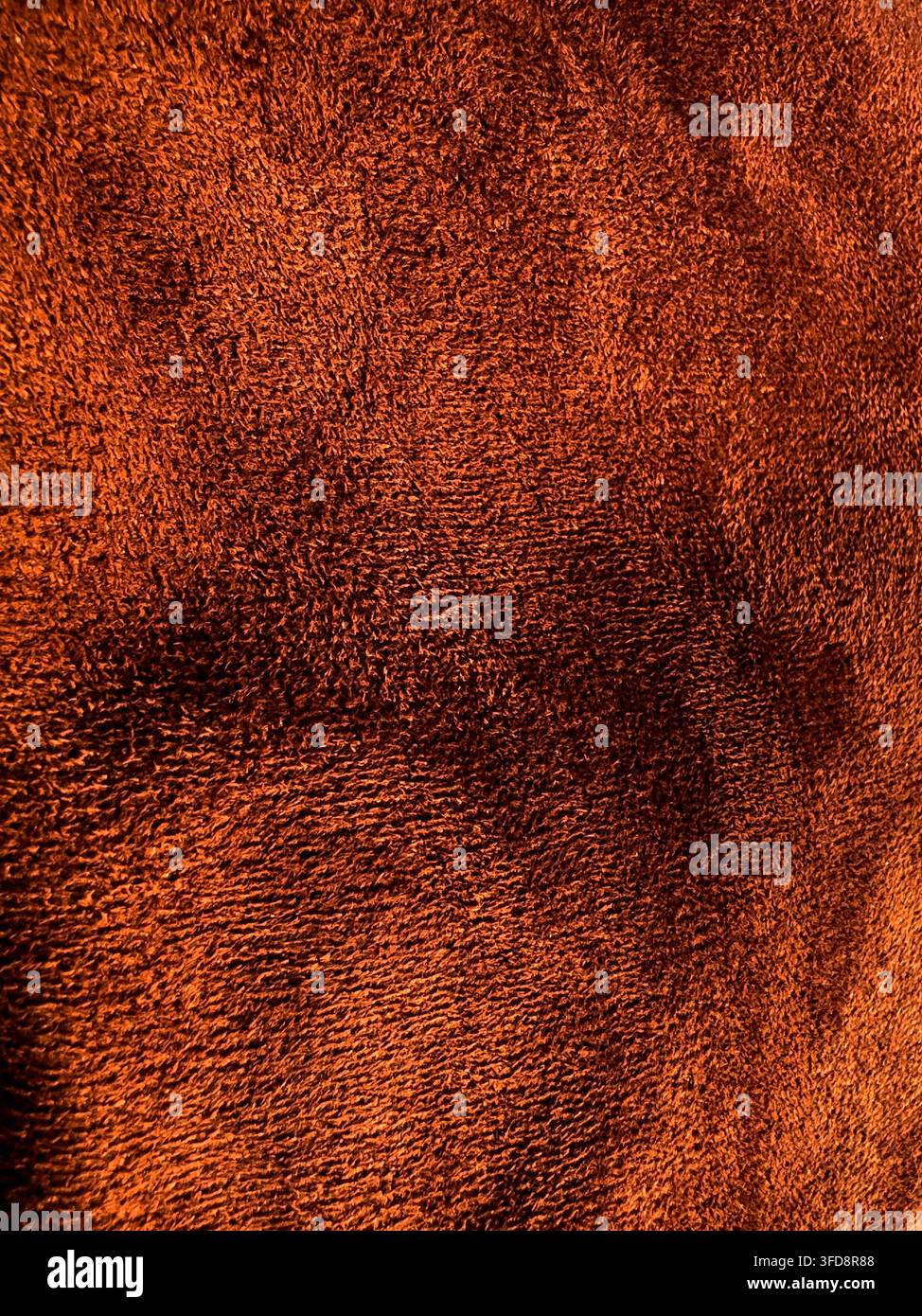 Nahaufnahme einer Textur, die weichen, warmen orangefarbenen Stoff mit feinen Details bei Innenbeleuchtung zeigt Stockfoto