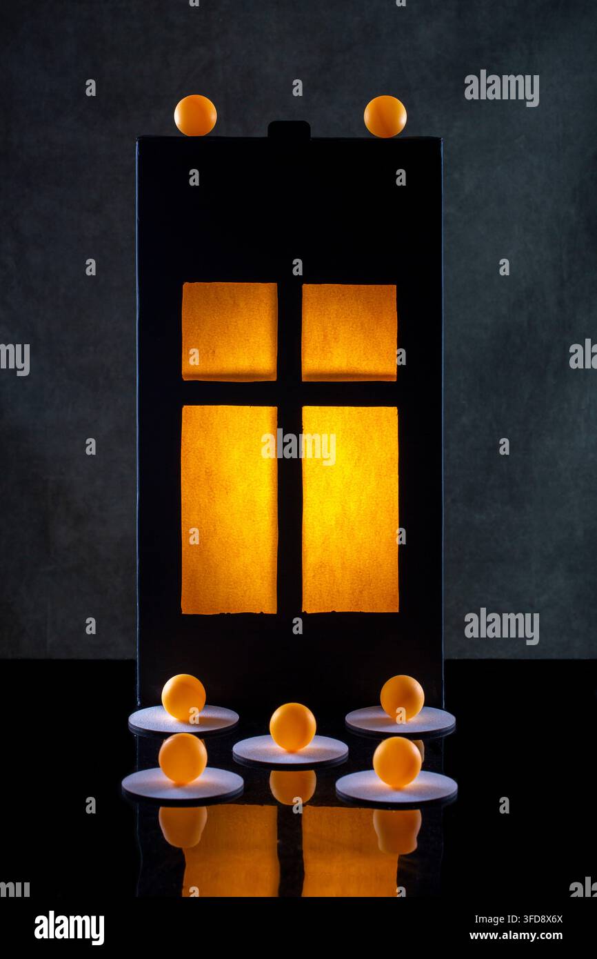 Silhouette eines leuchtenden Fensters, orangefarbene Kugeln auf dunklem Hintergrund Stockfoto