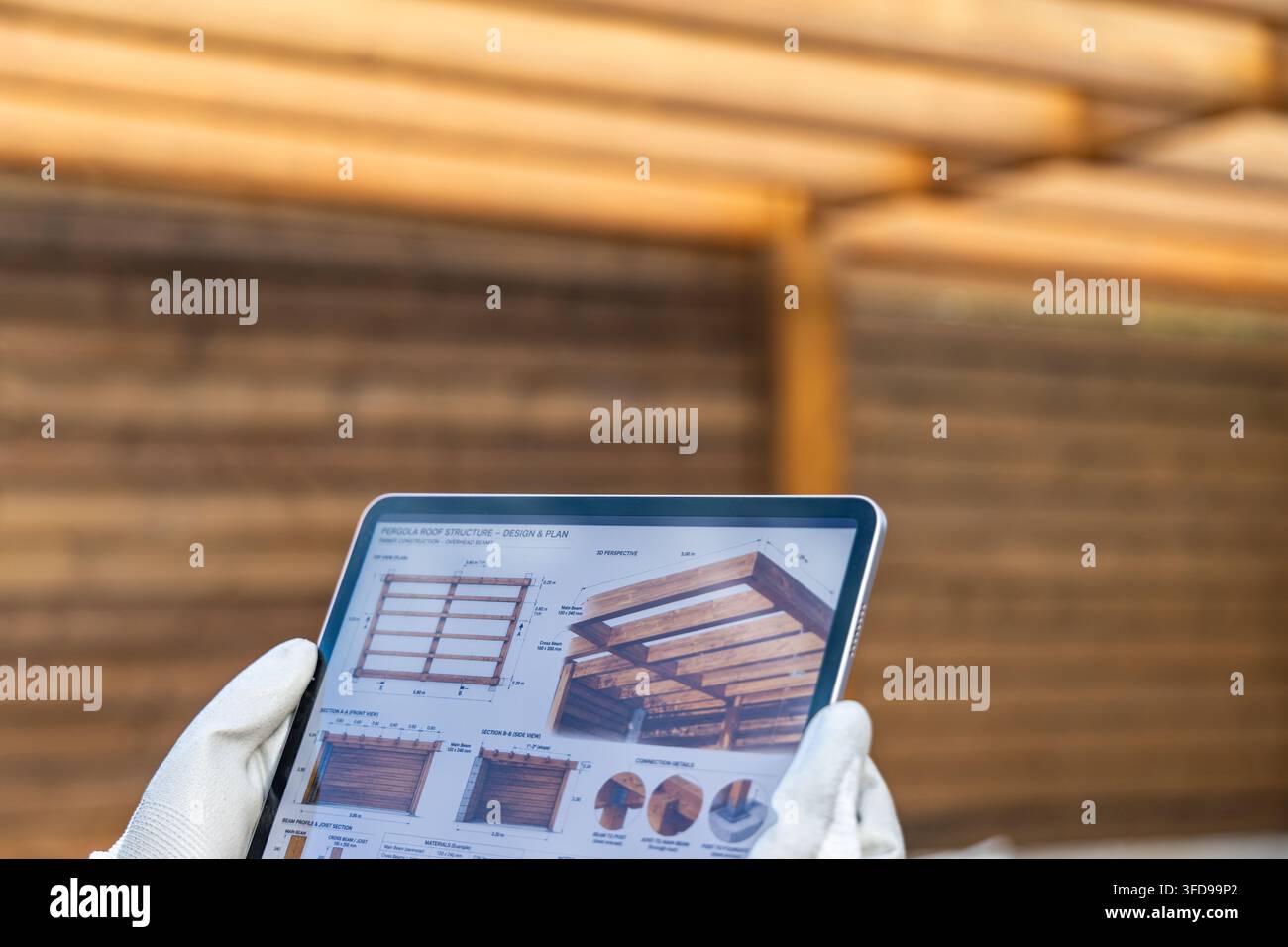 Eine Person mit weißen Handschuhen hält ein Tablet, das detaillierte Baupläne und 3D-Darstellungen einer hölzernen Pergoladachkonstruktion anzeigt Stockfoto