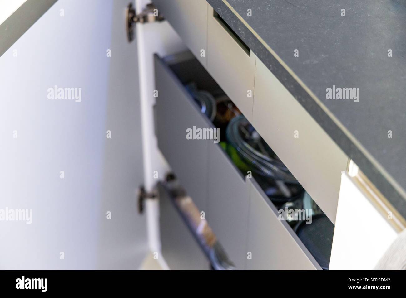 Eine Nahaufnahme eines modernen Küchenschranks mit geöffneten Türen und Schubladen, die die ordentliche Organisation im Inneren präsentieren Stockfoto
