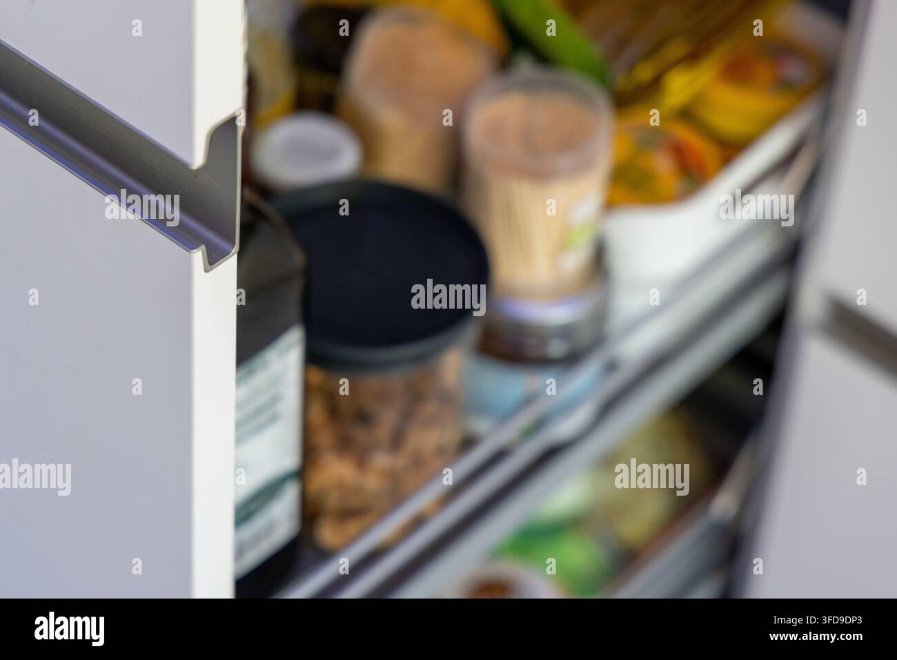 Eine Nahaufnahme eines offenen Kühlschranks, der organisierte Regale mit Gläsern, Flaschen und Lebensmitteln zeigt Stockfoto