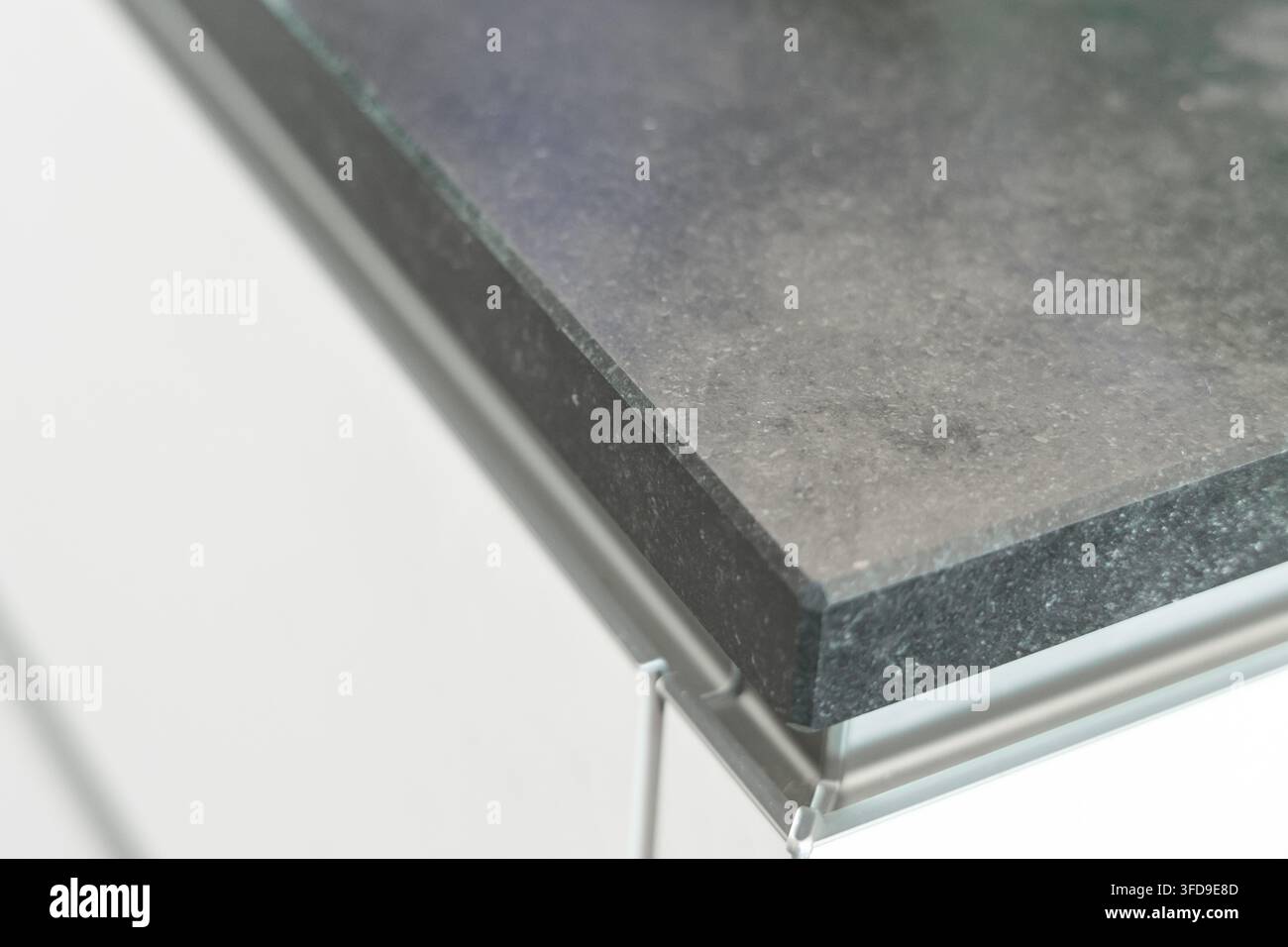Eine detaillierte Ansicht einer polierten dunklen Granitfläche mit subtilen Sprenkeln und einem eleganten Metallkanten detail auf einem sauberen weißen Hintergrund Stockfoto