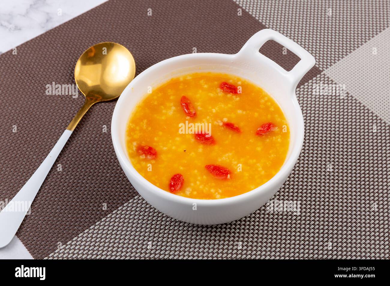 Goldener Hirse-Kürbisbrei garniert mit getrockneten Goji-Beeren Stockfoto