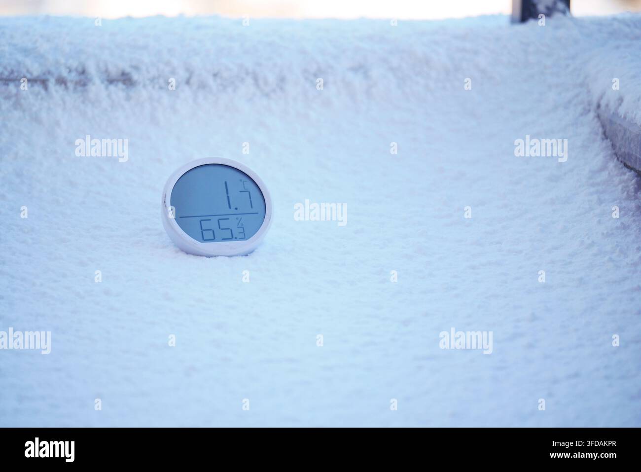Runder weißer digitaler Thermometer und Hygrometer, der auf einer schneebedeckten Oberfläche liegt Stockfoto