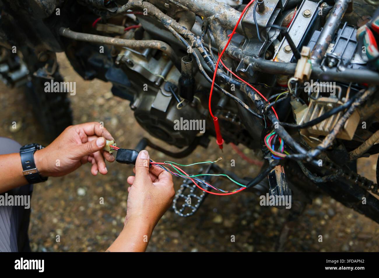 Ein Mechaniker repariert einen Motorradmotor im Freien mit freiliegenden elektrischen Kabeln und Werkzeugen Stockfoto