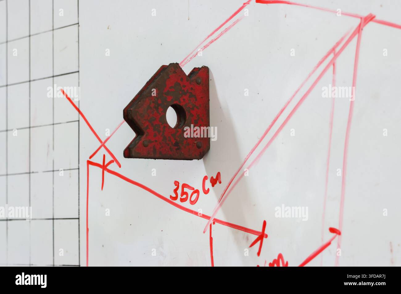 Ein roter magnetischer Schweißwinkelhalter auf weißer Tafel mit handgezeichnetem Messdiagramm und Konstruktionsskizze Stockfoto