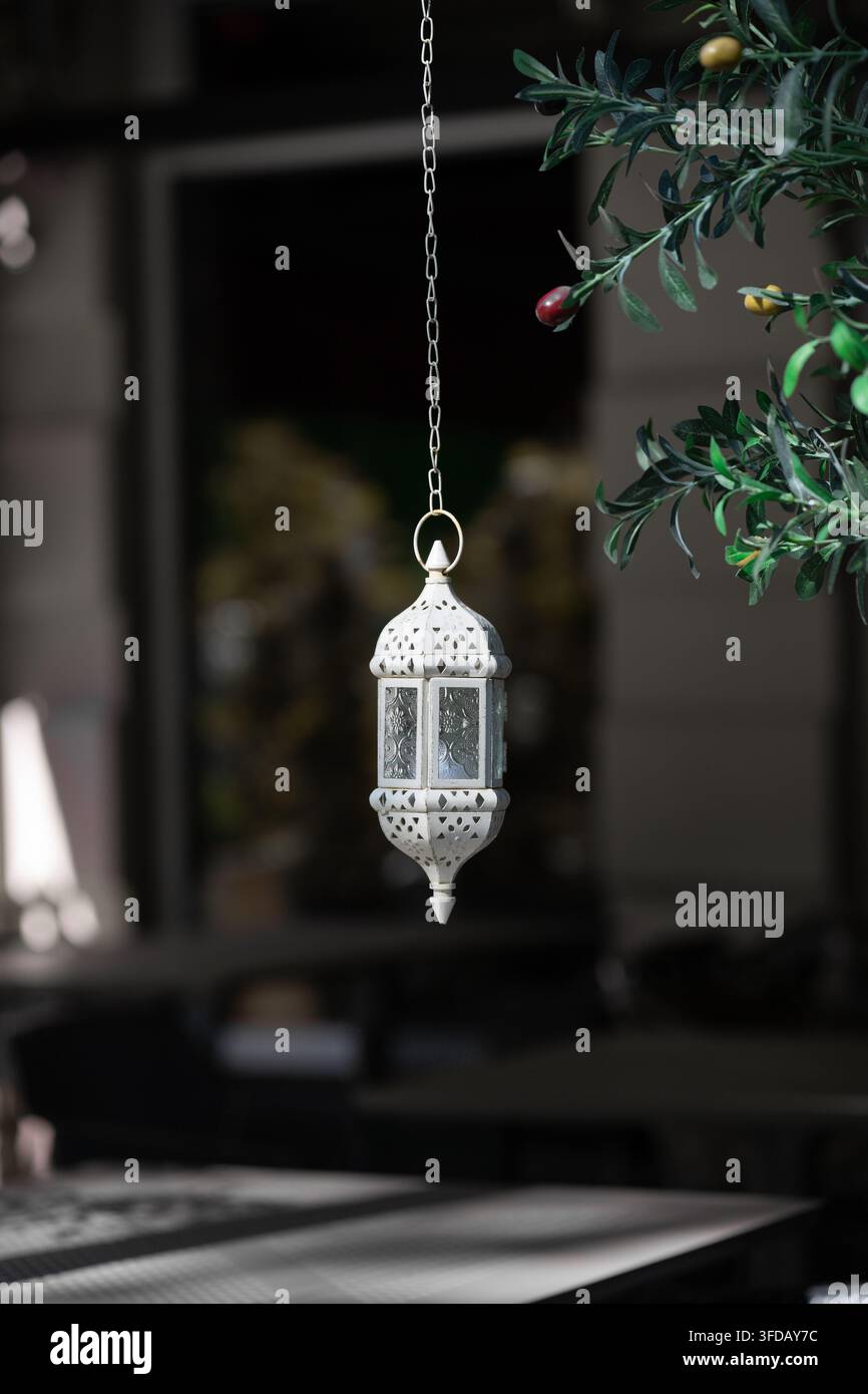 Vertikale Nahaufnahme einer traditionellen arabischen oder indischen geschnitzten Lampe vor einem unscharfen dunklen Terrassenhintergrund. Sauberes minimalistisches orientalisches Designpatte Stockfoto