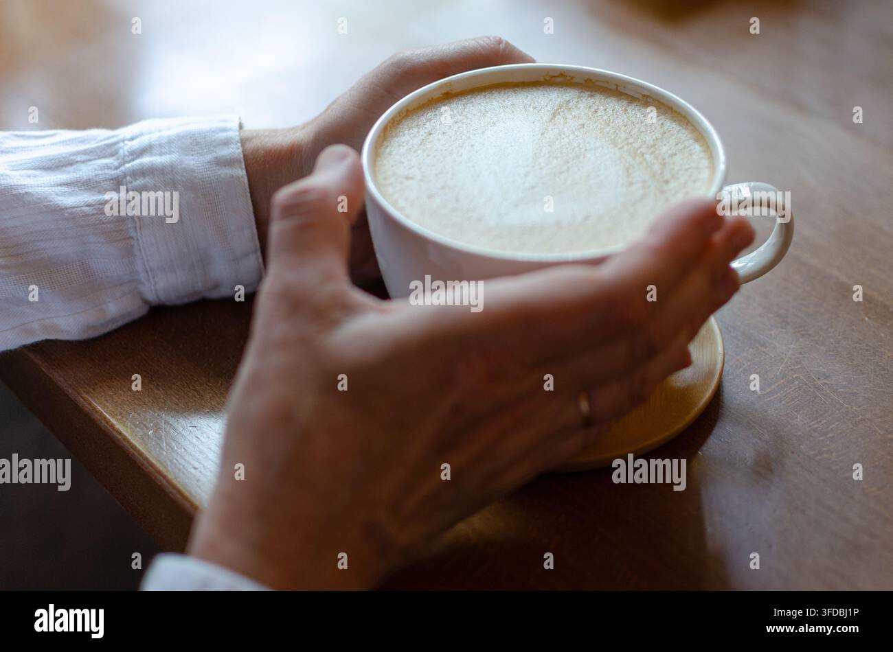 Nahaufnahme von Händen, die eine weiße Tasse Cappuccino halten Stockfoto