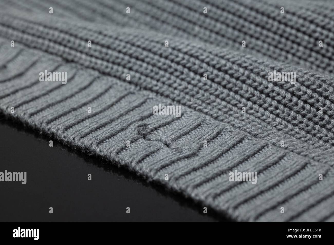 Grauer gestrickter Wollstoff, der ein Rippenmuster und eine weiche Textur zeigt Stockfoto
