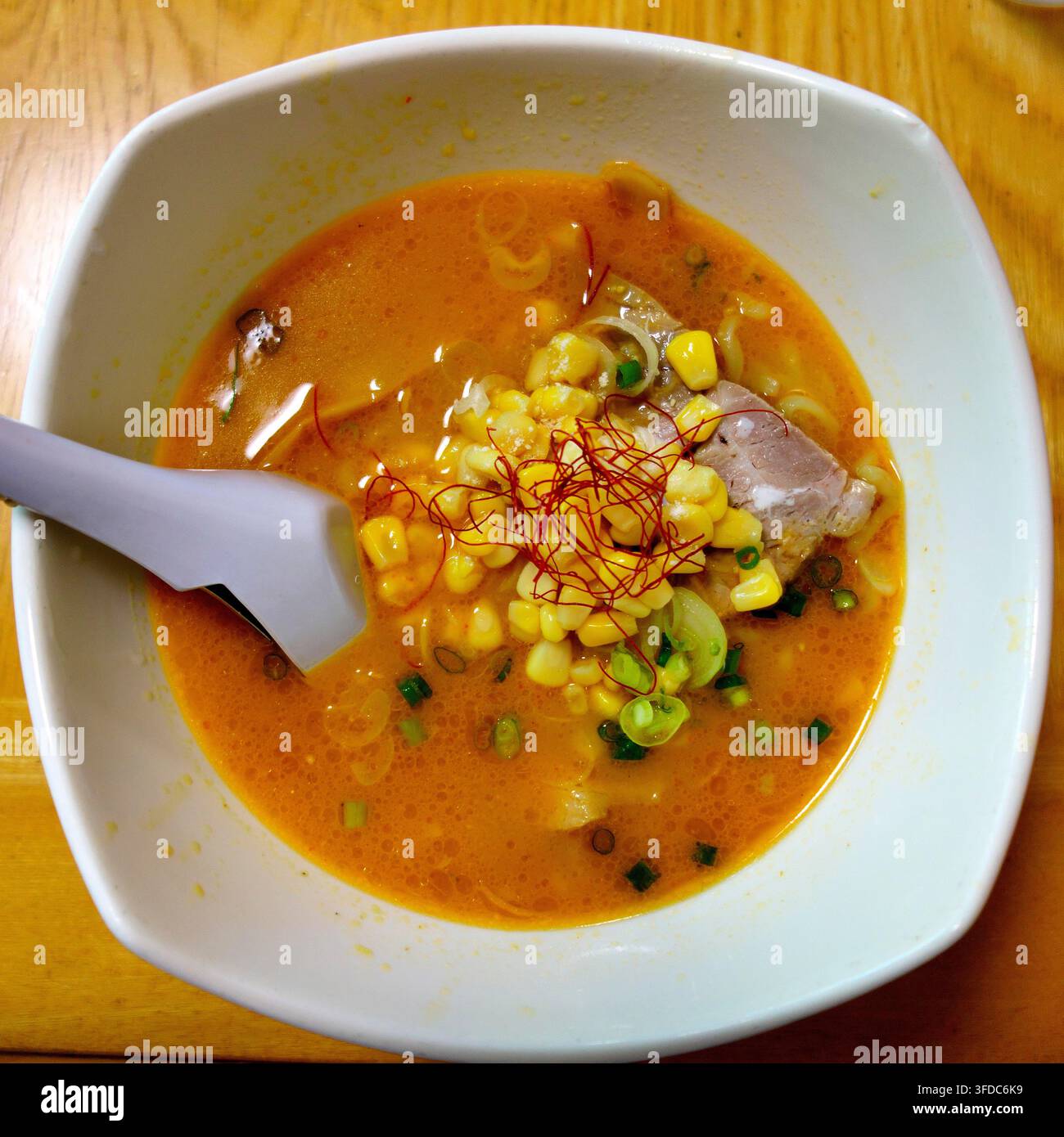 Leckere japanische Miso-Ramen-Nudeln serviert in einer weißen Schüssel, belegt mit süßer Maiskolben, geschnittenem Chashu-Schinken, grüner Zwiebel und roten Chilifäden in Stockfoto