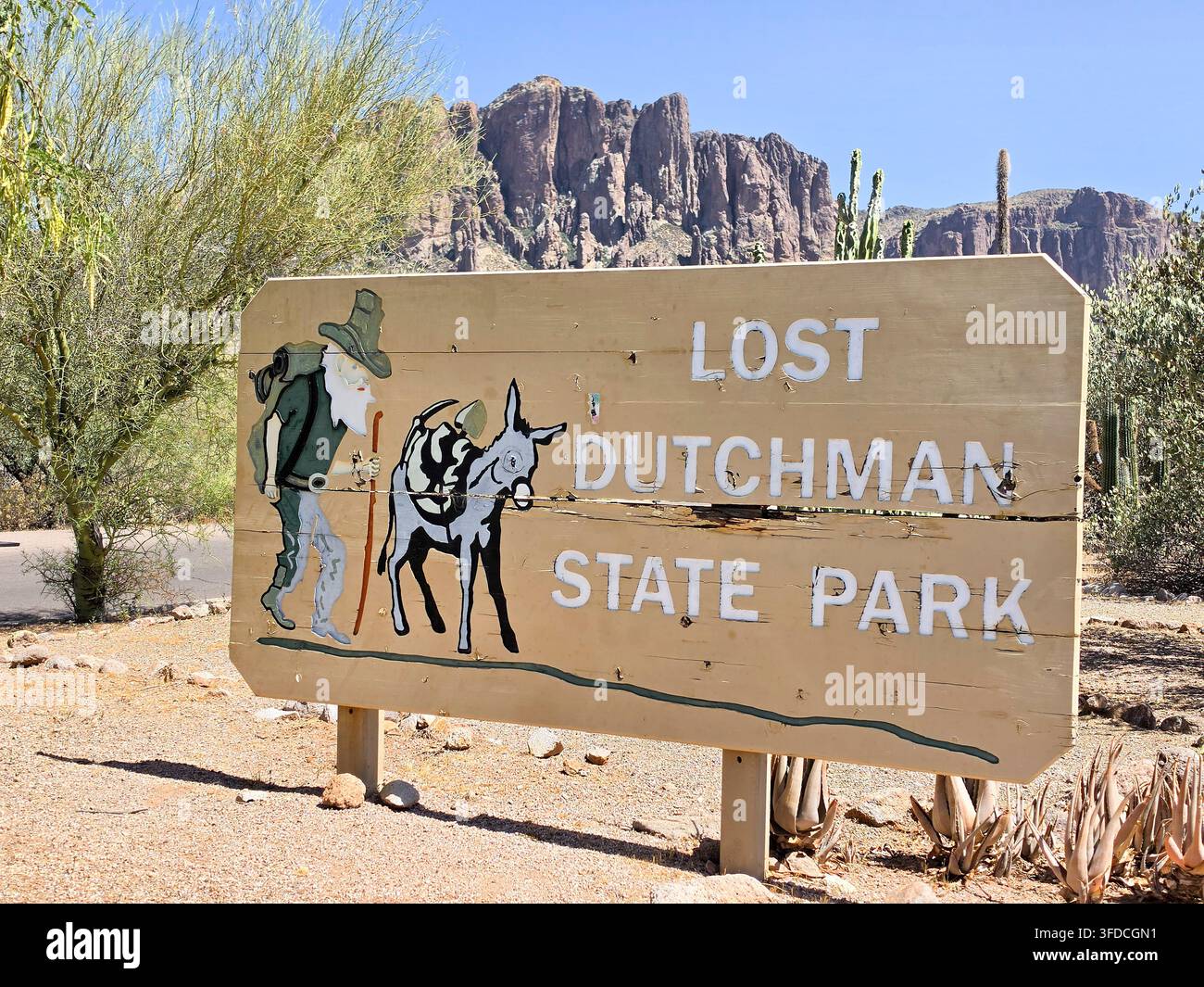 Eingangsschild des Lost Dutchman State Park in Arizona, USA, mit Bild eines Mannes und eines Esels; im Hintergrund die Superstition Mountains und Palo-Verde-Bäume Stockfoto