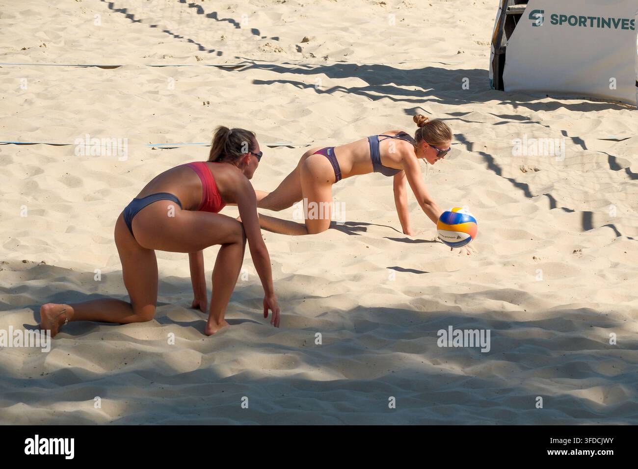 KIEW, UKRAINE – 15. AUGUST 2026: Zwei Amateur-Beachvolleyballspielerinnen tauchen und rutschen auf dem Sandplatz, um einen tiefen Ball zu verteidigen. Die Athletinnen zeigen Stockfoto