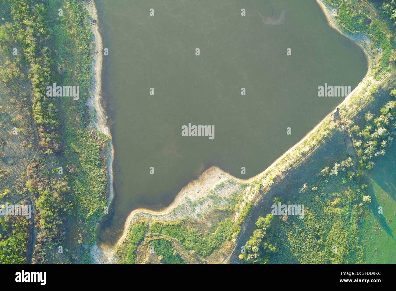 Ruhige Wasseroberfläche eines ländlichen Reservoirs, begrenzt von einem Stahlbeton-Damm und üppiger Vegetation, die Synergie von Natur und technischem Wassermanagement einfangend. Stockfoto