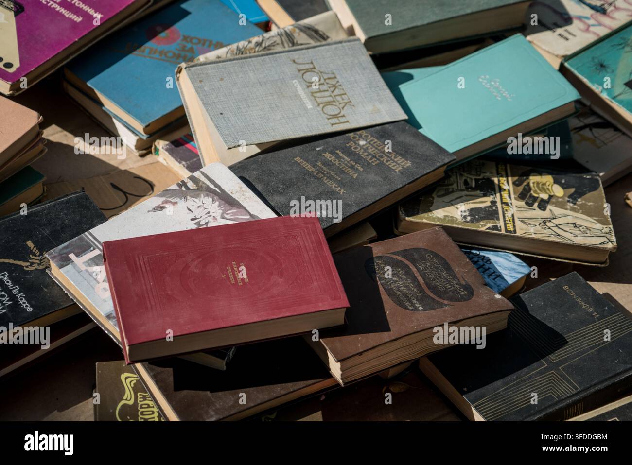 Eine Nahaufnahme aus Vogelperspektive zeigt einen wirren Stapel alter Bücher mit abgenutzten Einbänden in verschiedenen Blautönen, Grau, Kastanienbraun und Braun. Lesbarer Titel Stockfoto