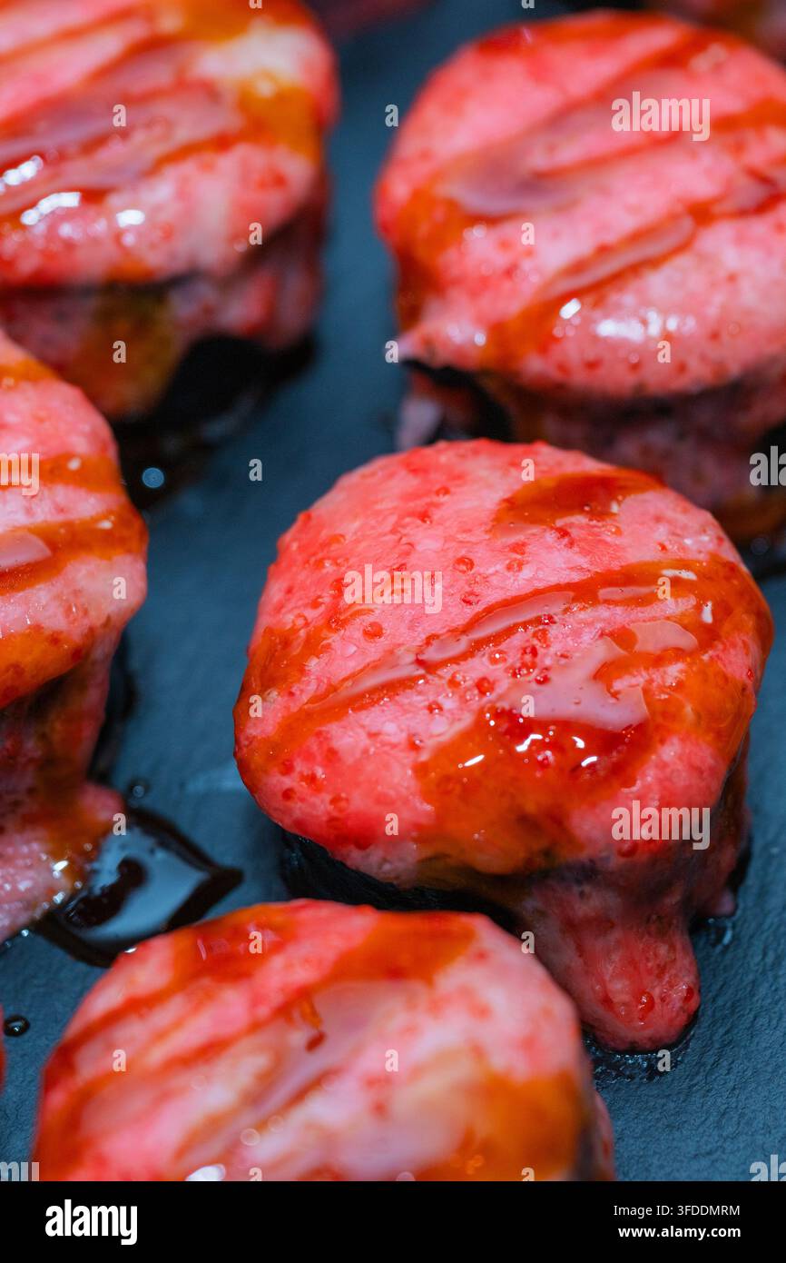 gebackene oder gegrillte Sushi-Rollen, die mit einer rosa cremigen Sauce und süßer Sojasauce überzogen sind. Stockfoto