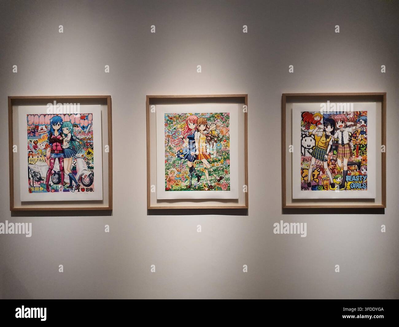 Drei gerahmte Anime-Kunstwerke, die an einer weißen Galeriewand ausgestellt sind. Der linke Rahmen enthält eine Illustration von zwei weiblichen Charakteren mit blau und Stockfoto