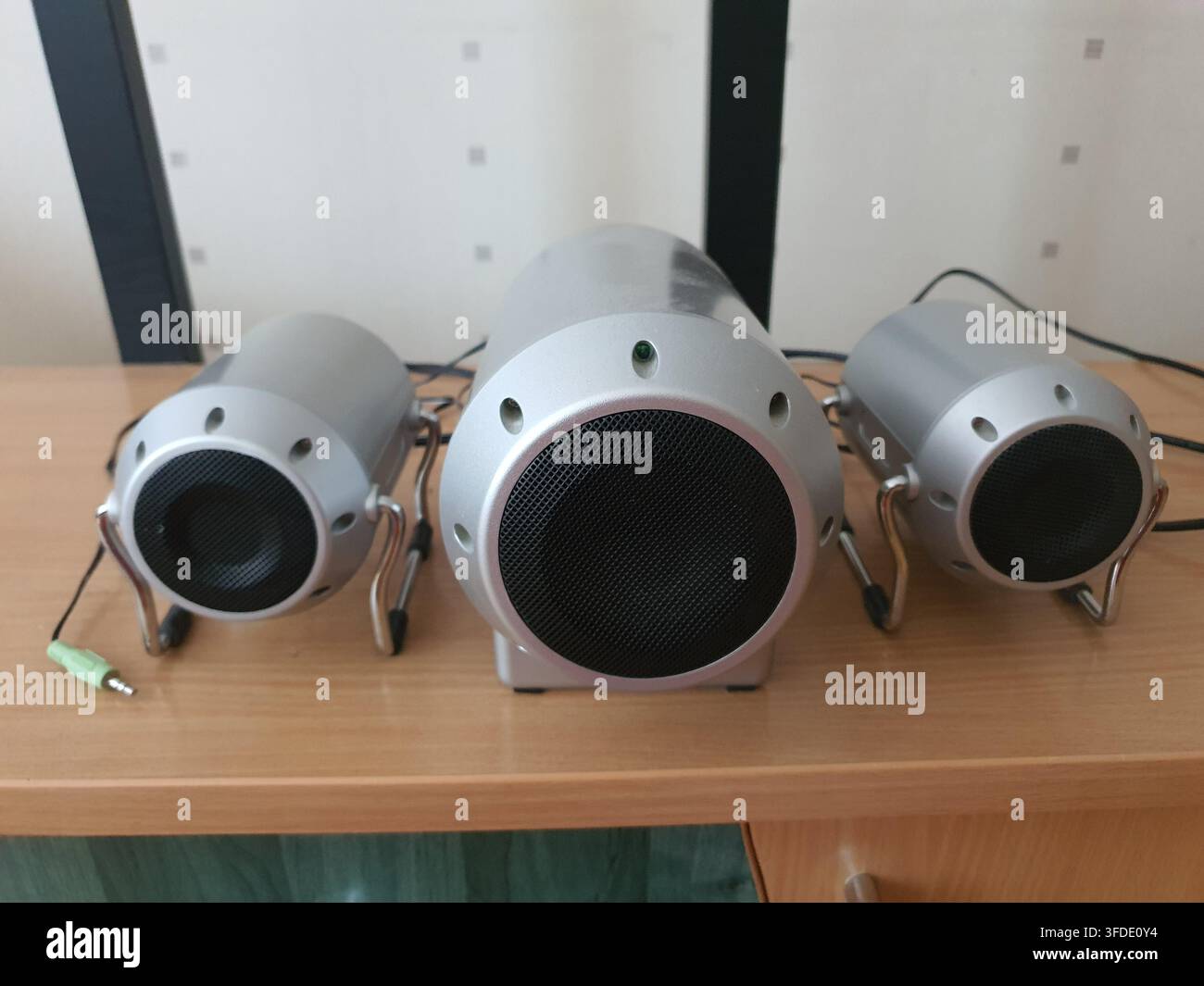 Drei zylindrische silberne Multimediakolben, die auf einer hellen Holzschreibtischfläche positioniert sind, bestehend aus einer größeren zentralen Subwoofer-Einheit, flankiert von Stockfoto