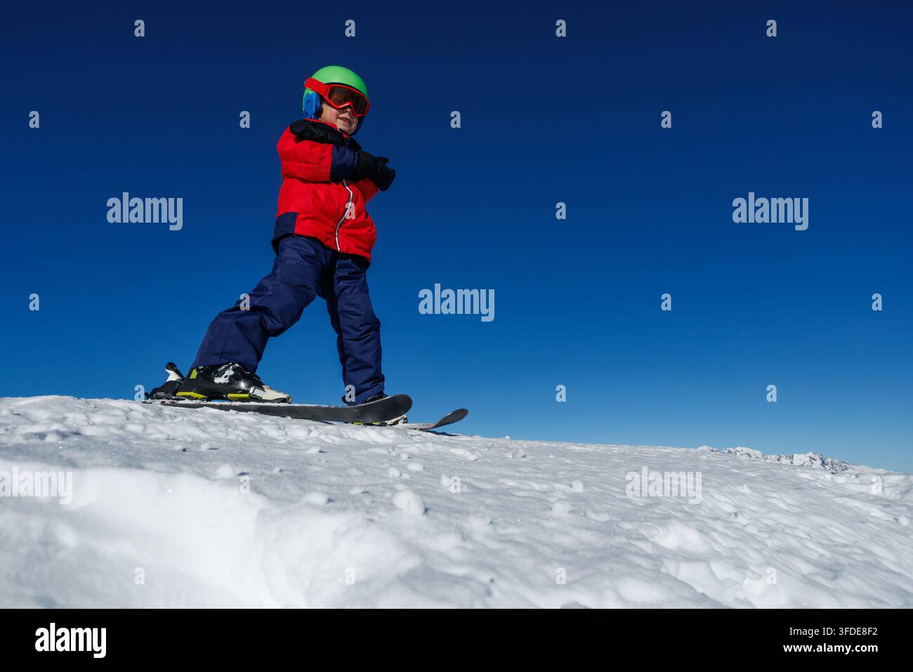 Selbstbewusster Jungskifahrer fährt über schneebedeckte Pisten unter blauem Himmel Stockfoto
