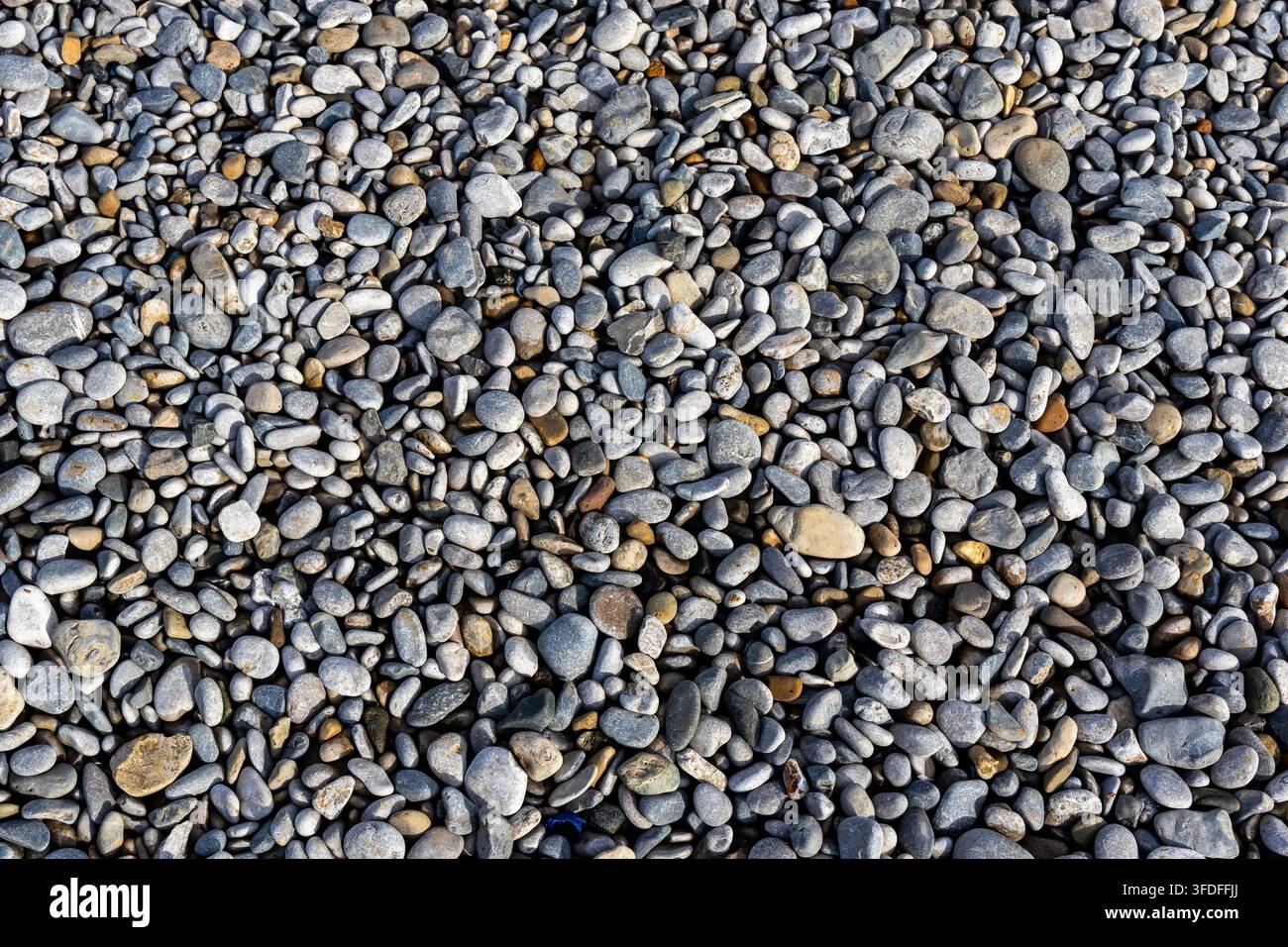 Abstrakte Hintergrundansicht von glatten, abgerundeten Kieselsteinen und Steinen, die eine Strandoberfläche mit natürlichem Kontrastdetail bedecken Stockfoto