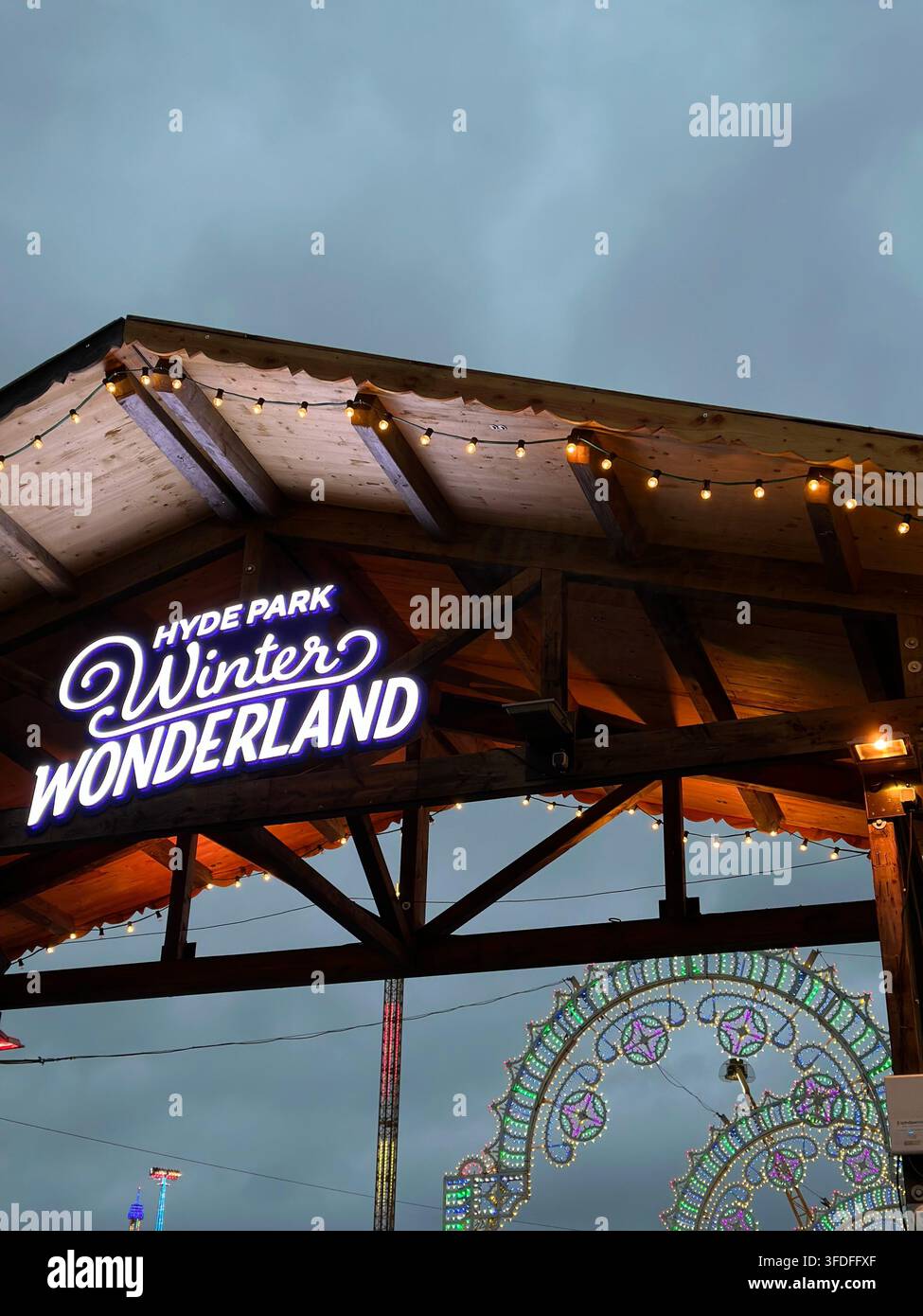 Beleuchtetes Hyde Park Winter Wonderland-Eingangsschild unter einem hölzernen Dach mit festlichen Lichtinstallationen bei Nacht während Weihnachten in London, UK. - Smartphone-aufgenommenes Stockfoto