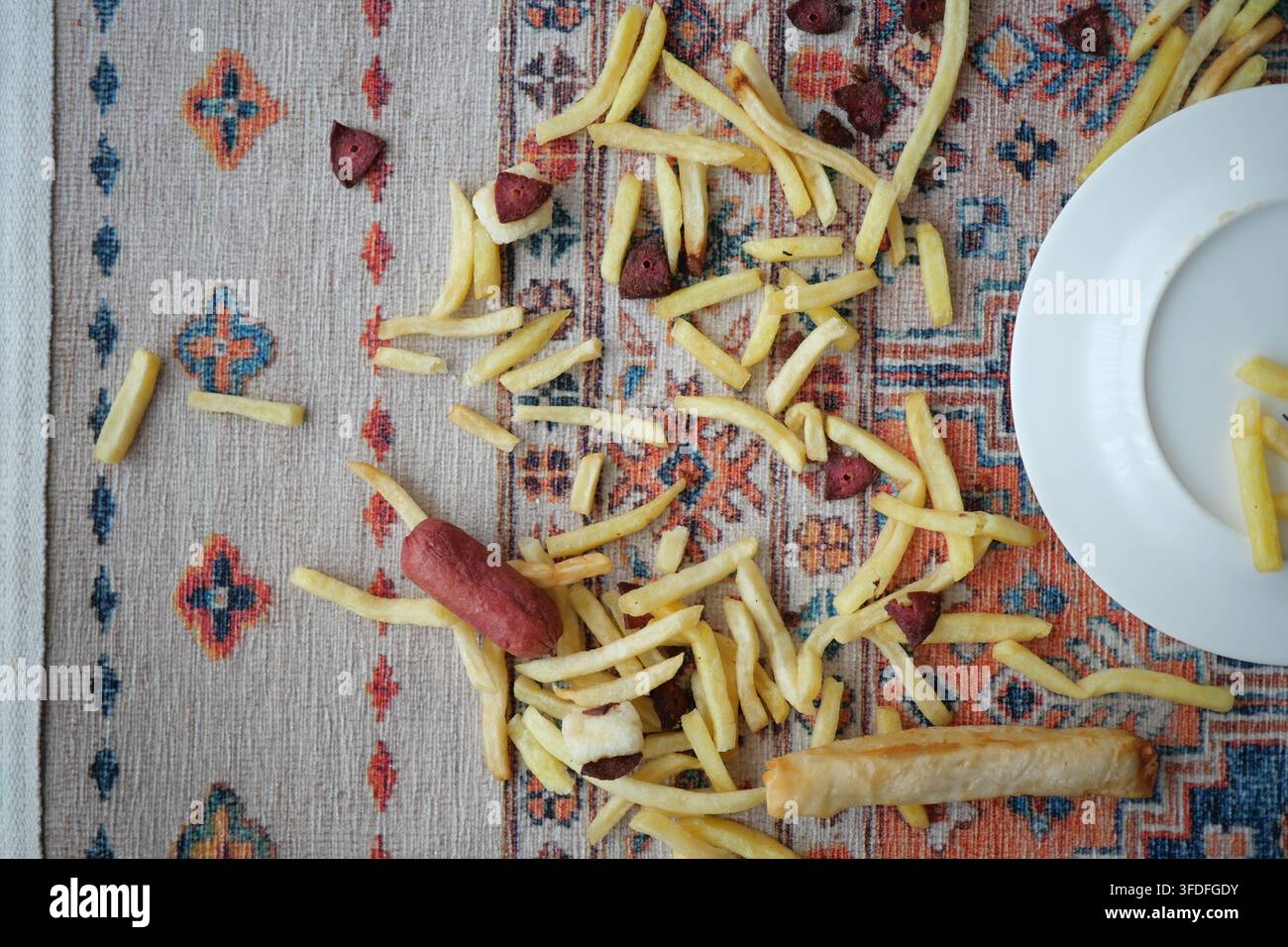 Verstreute Pommes und ein Hotdog auf einem gemusterten Teppich Stockfoto