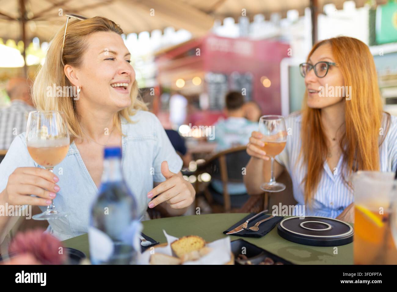 Zwei Freunde genießen Getränke und Essen in einem Straßencafé in einer geschäftigen städtischen Umgebung an einem sonnigen Tag Stockfoto