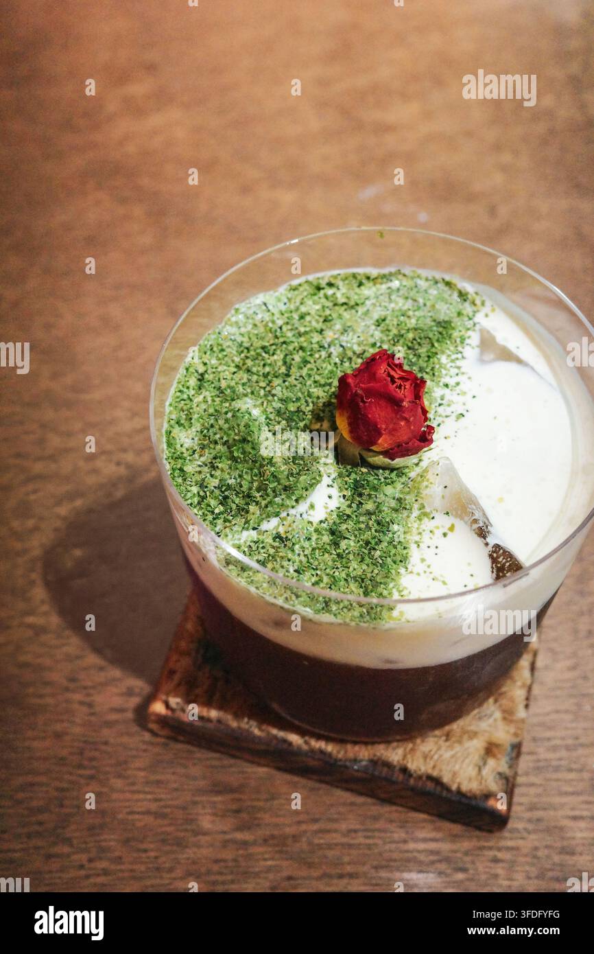Eine Aufsichtaufnahme von dunklem Kaffee und weißem Milchschaum in einem durchsichtigen Glas. Die Oberfläche des Milchschaums ist mit smaragdgrünem Matcha-Pulver bestreut Stockfoto