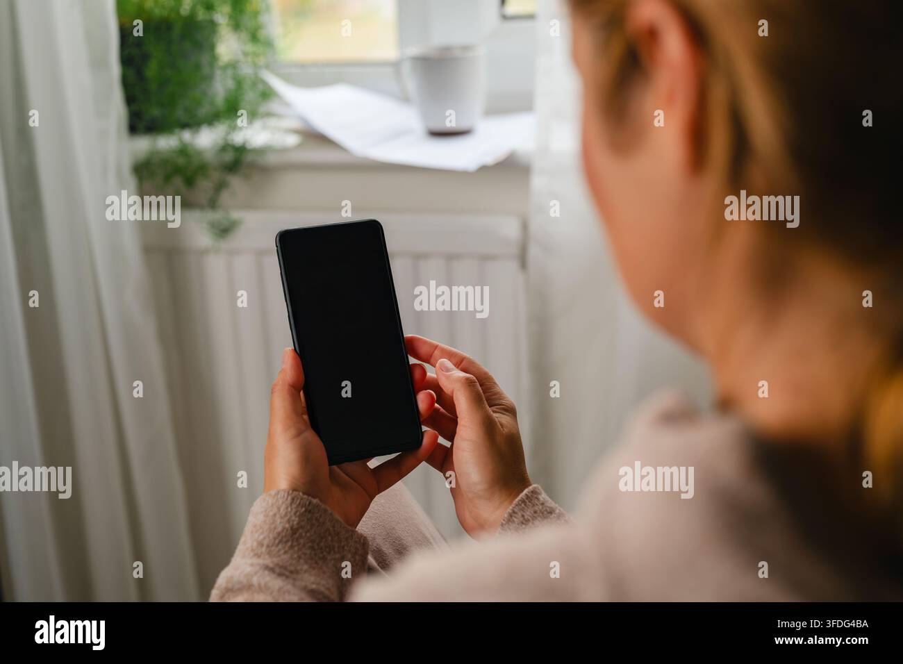 Über-Schulter-Ansicht einer Frau, die zu Hause ein Telefon benutzt Stockfoto