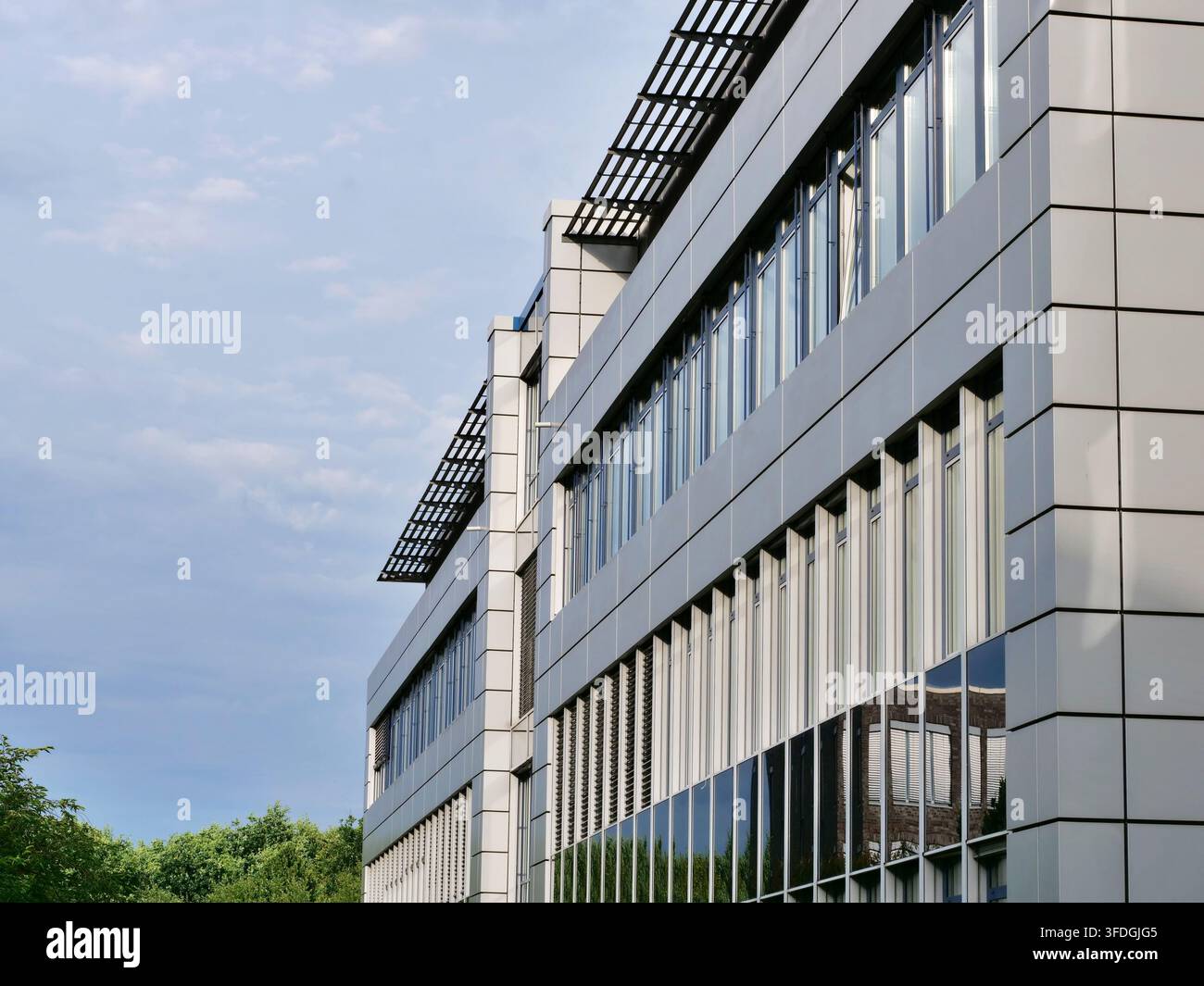 Weitwinkel-Perspektivenaufnahme eines mehrstöckigen modernen Bürogebäudes mit hellgrauer Paneelverkleidung, dunkel getönten Fenstern mit Reflexionen und Sonnenschutz Stockfoto