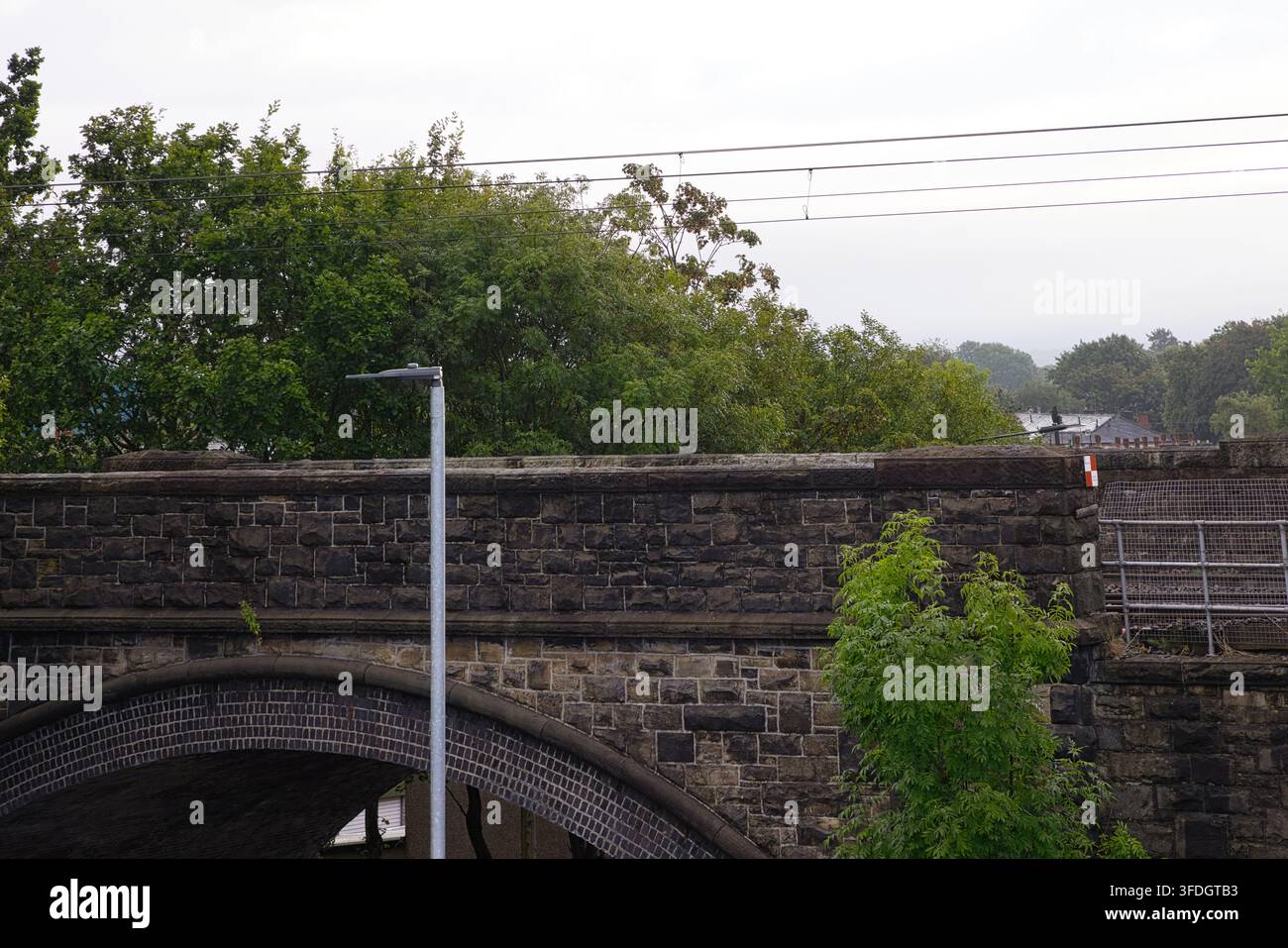 Steinerne Brücke, die Gleise einer Leichtbahn über Spring Lane trägt, vor einem Hintergrund von Bäumen in Radcliffe, Lancashire, UK. Stockfoto