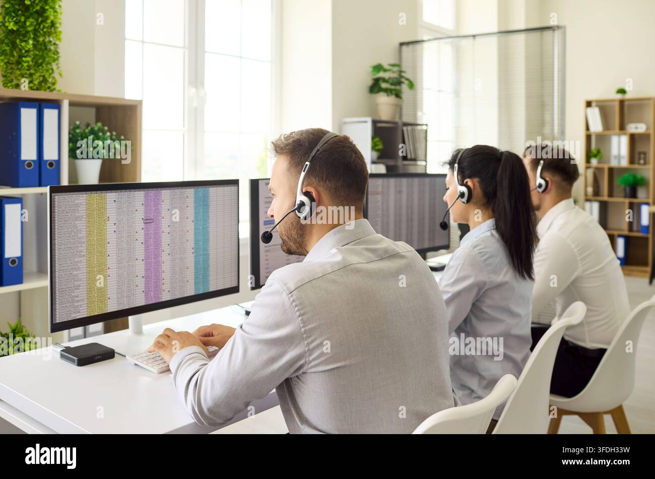 Konzentrierte Callcenter-Mitarbeiter, die Headsets an Monitoren in einem modernen Büro verwenden Stockfoto