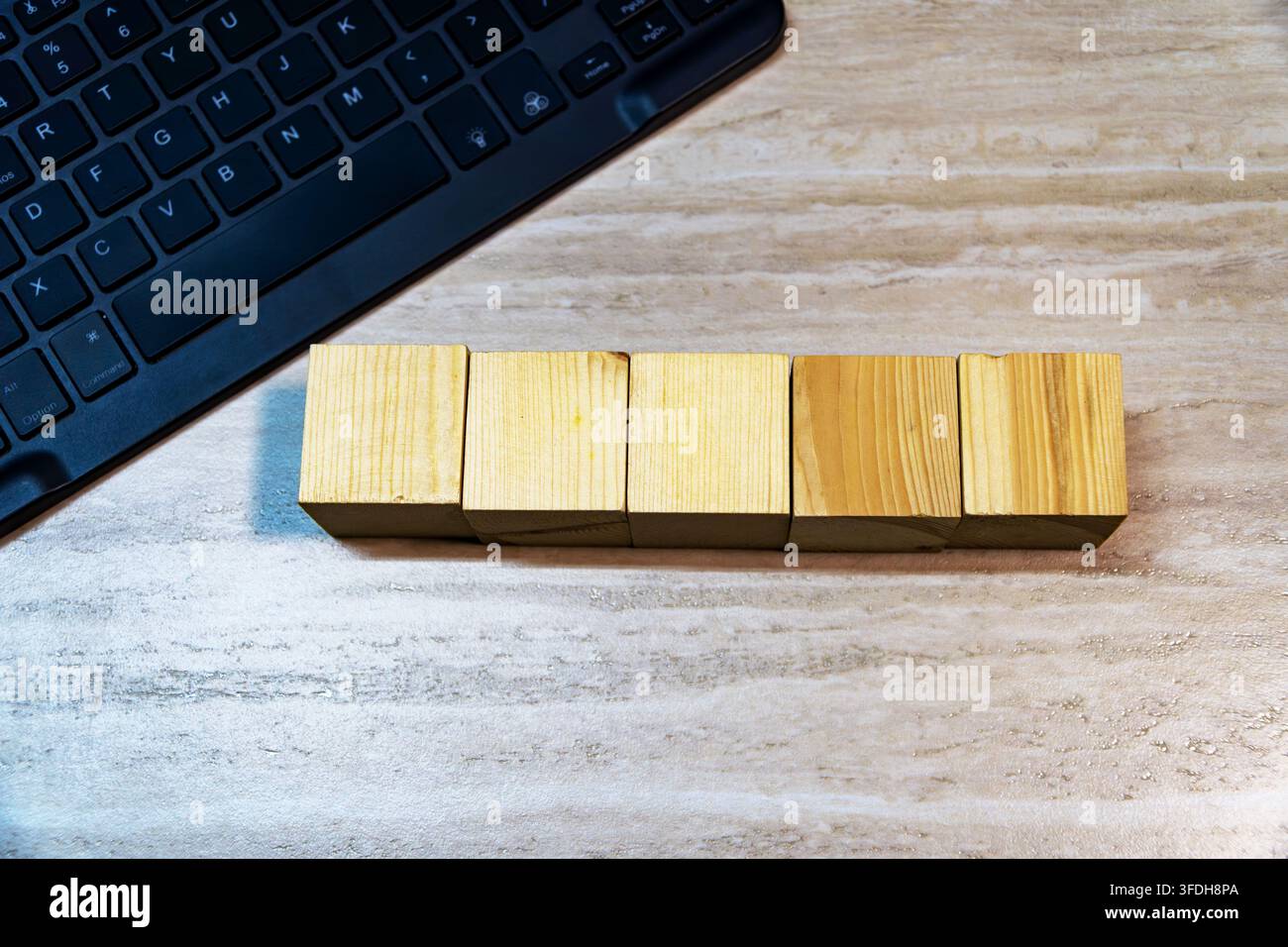 Oberansicht von fünf leeren Holzwürfeln in einer Reihe neben einer schwarzen Computertastatur auf einem Holzschreibtisch. Kopierraum für Text oder Mockup. Stockfoto