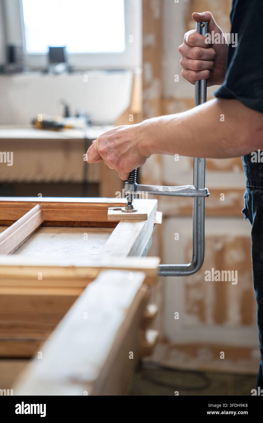 Handwerker an der Werkbank in der Restaurierungswerkstatt, der Teile eines alten Holzfensterrahmens mit einer Klemme befestigt Stockfoto