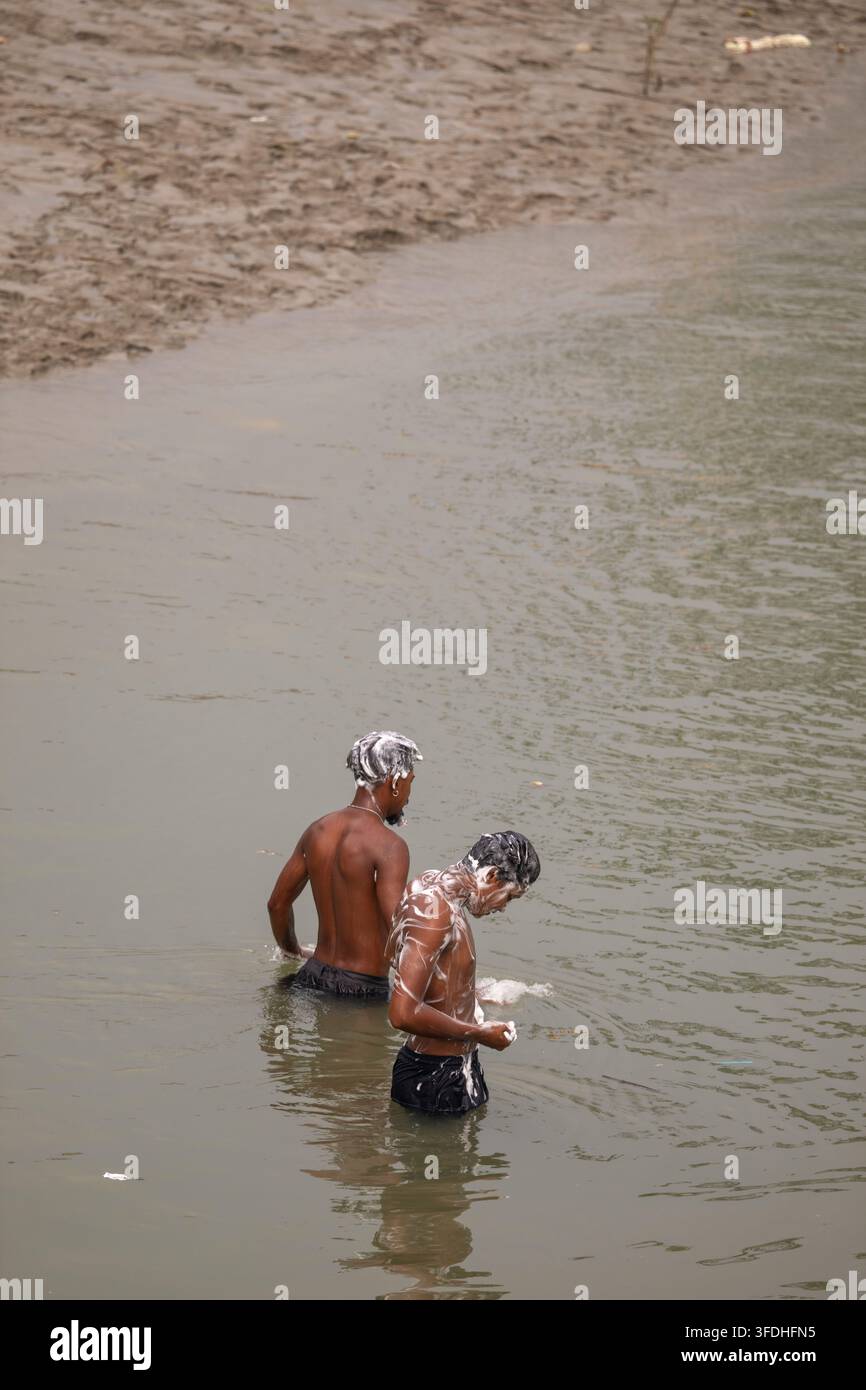 Männer, die sich in einem trüben Fluss waschen, bedeckt mit Seifenschaum und Schaum, was ein tägliches Ritual in einer natürlichen Umgebung unterstreicht Stockfoto