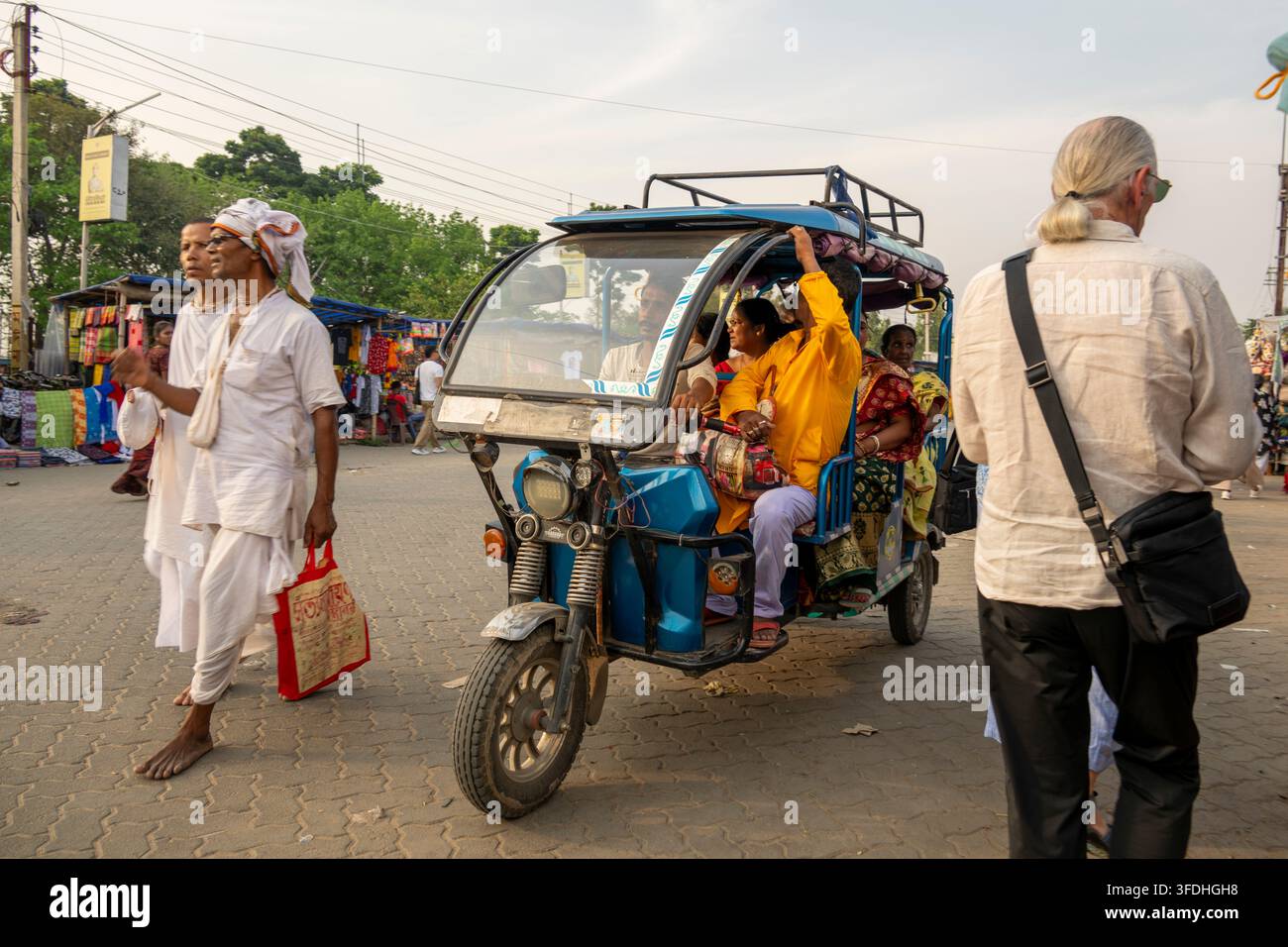 Eine Gruppe von Menschen in traditioneller indischer Kleidung wird gesehen, wie sie auf einer Straße gehen und in einem elektrischen Rickshaw fahren Stockfoto