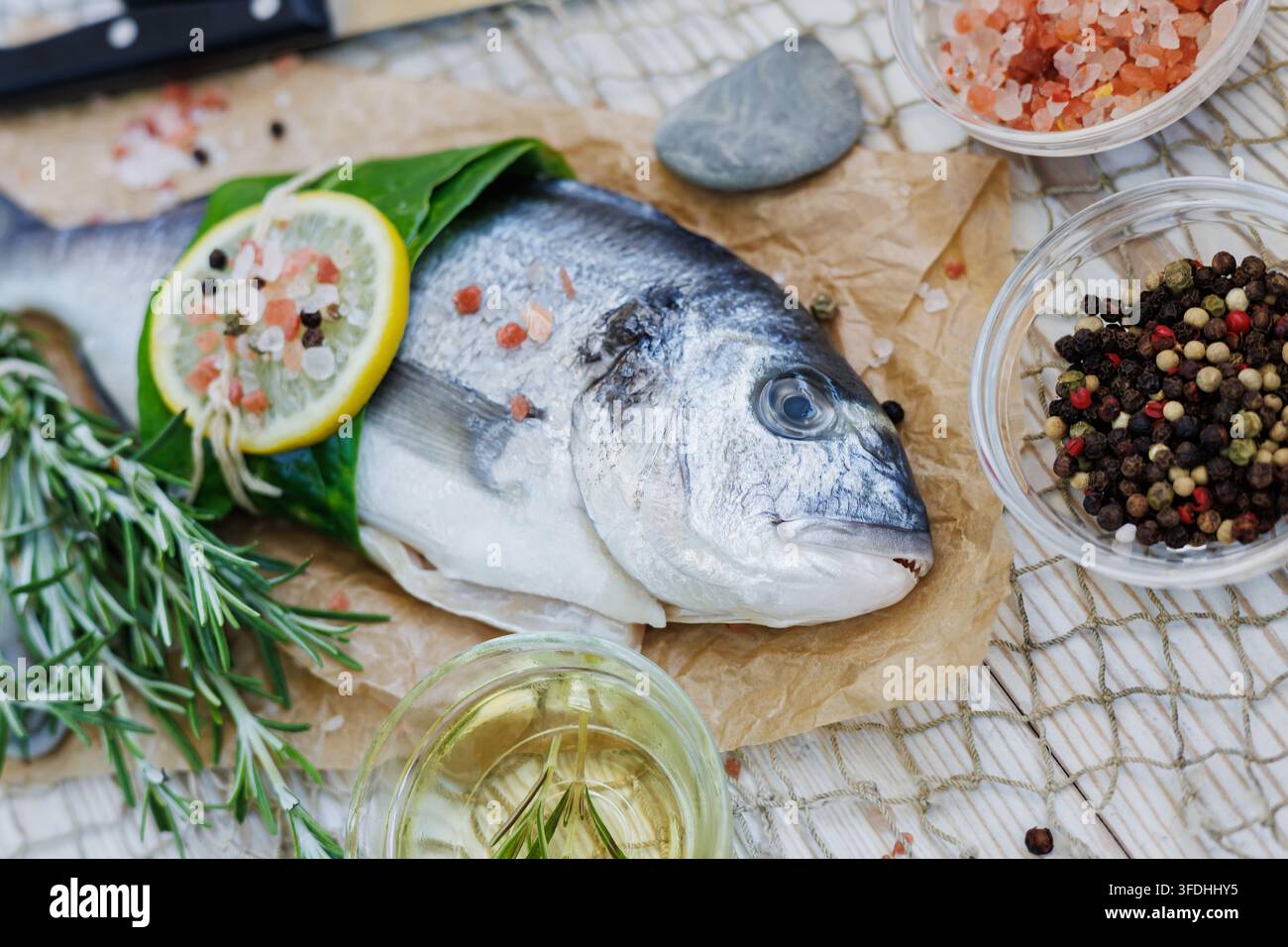 Premium-Roh-Spargel mit Rosmarin, Olivenöl, Zitrone, rosa Salz und gemischten Pfefferkörnern arrangiert für gesundes Meeresfrüchtekochen auf rustikalem Holz Stockfoto